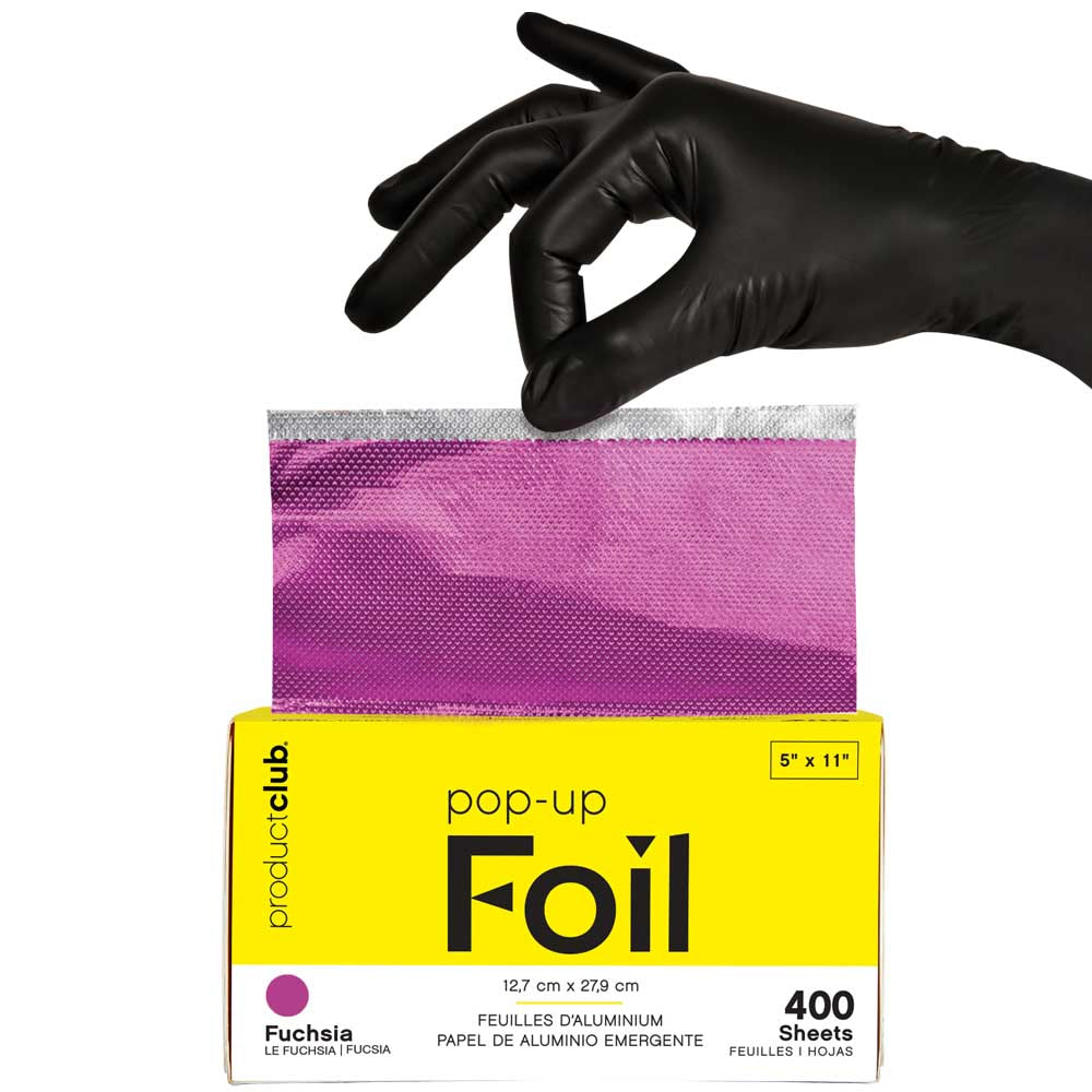 A hand wearing a black glove is placing a sheet of fuchsia aluminum foil into a yellow package labeled 'pop-up Foil' by product:club. The package indicates 400 sheets and shows a fuchsia color swatch.