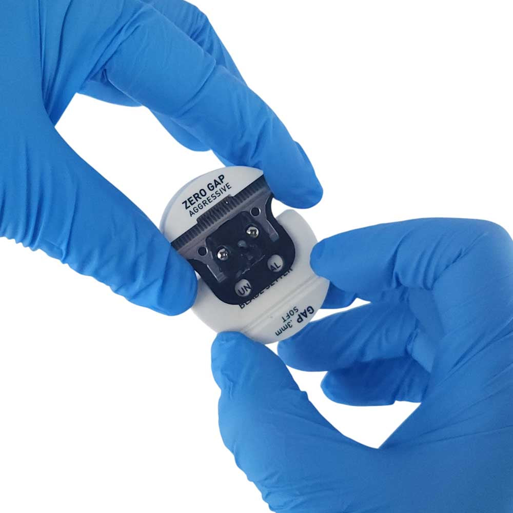 Blue gloved hands holding a small white and black round electronic device labeled 'ZERO GAP AGGREGATE' against a plain white background.