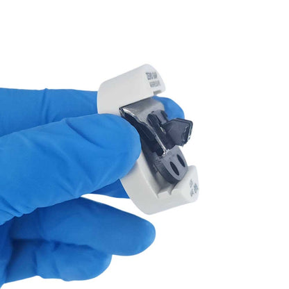 A hand wearing a blue nitrile glove holds a small white plastic component with a black and silver metal clip or connector against a plain white background.