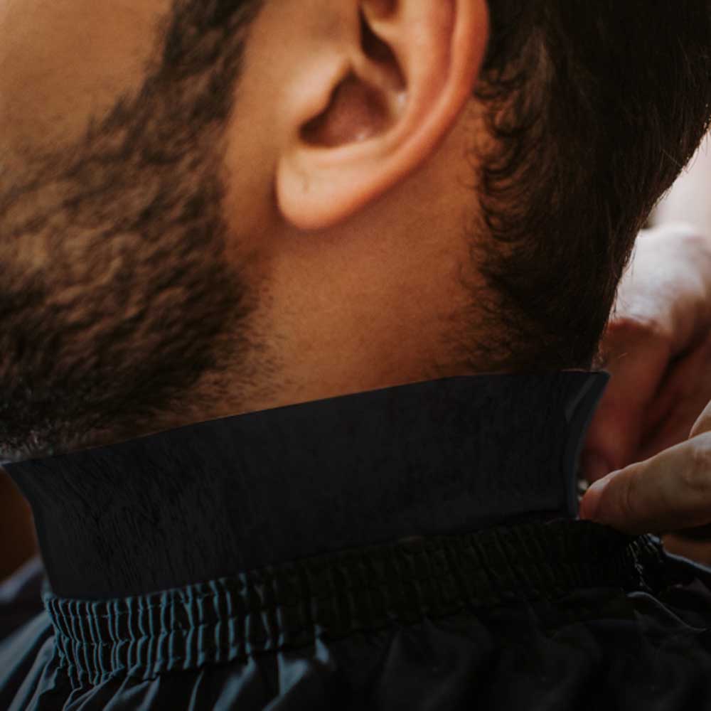 Close-up of a barber applying The Shave Factory Premium Black Neck Strip around a male client's neck.